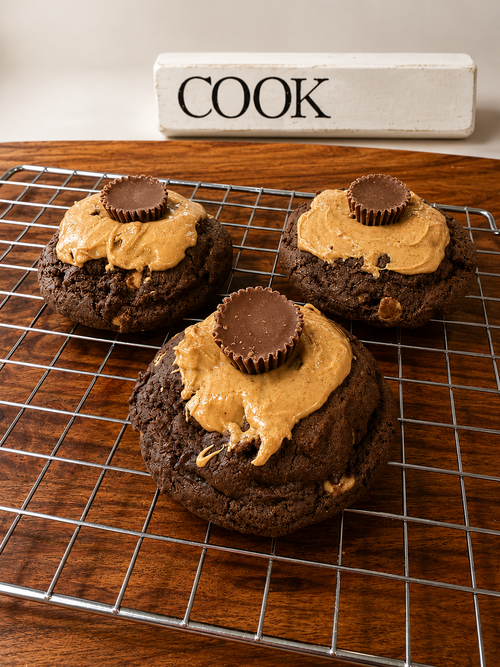 Choco PB Bomb Cookie topped with peanut butter drizzle and Reese's Peanut Butter Cup on a cooling rack